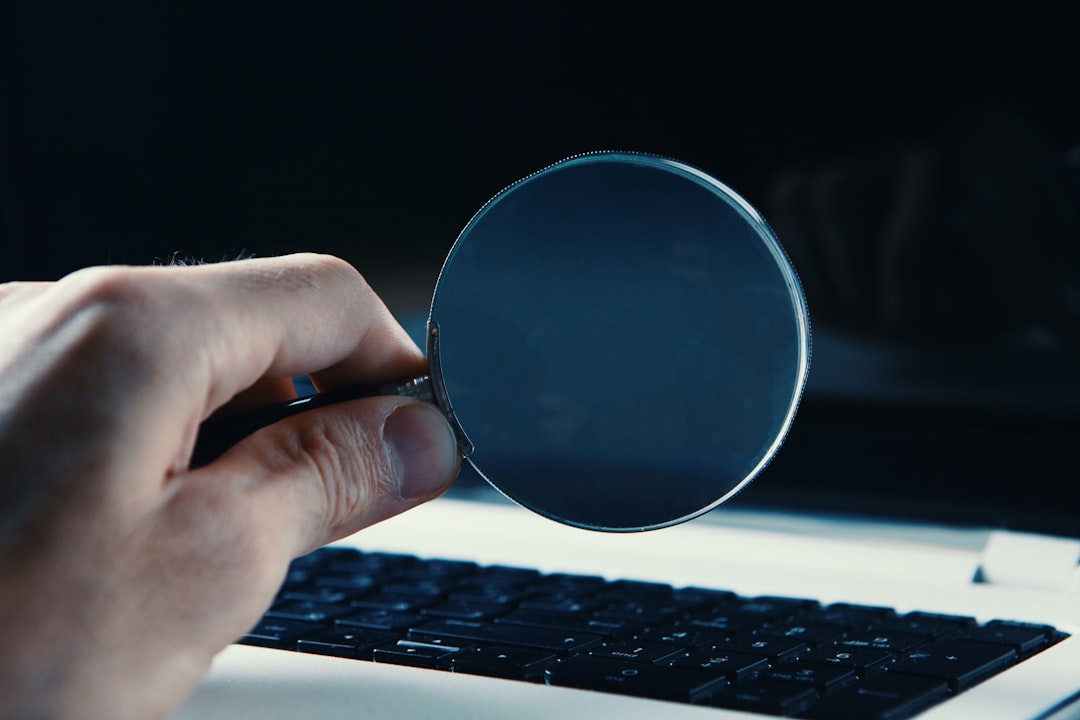 Hand holding a magnifying glass over a laptop keyboard